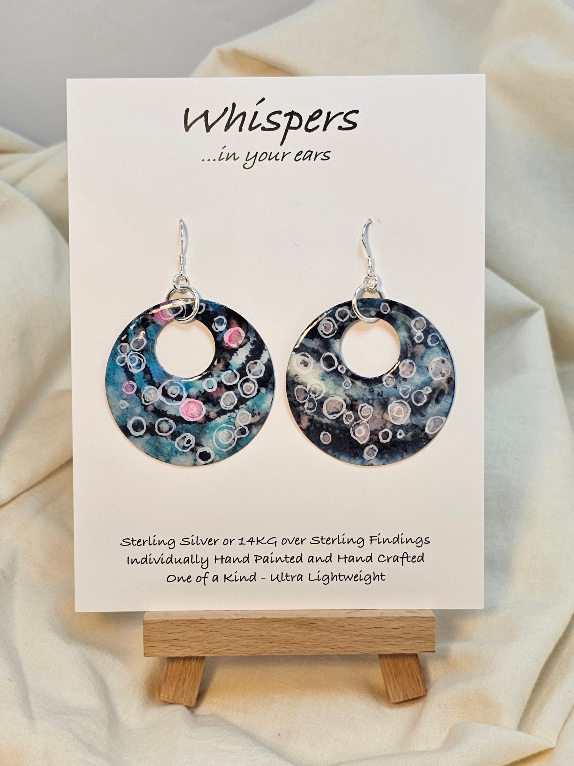 Bubbles Hand painted watercolor paper earrings. Ultra lightweight. Dark blue, pink, light pink, turquoise with white circles . Back is painted with similar color and design. Large circular in shape with circular cut out. Resin coating for durability. Sterling silver findings. Hangs 2" in Length