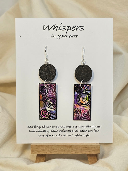 Black Spiral Motif Hand Painted Paper and Wood Earrings. 3/4" x 1 5/8" Paper Rectangle hand painted brightly colored background with black swirl accents. Edged in black. Hanging from embellished wooden disc painted black. Back is painted to match. Resin coating for durability. Sterling Silver findings. Hangs 2 1/2" in length