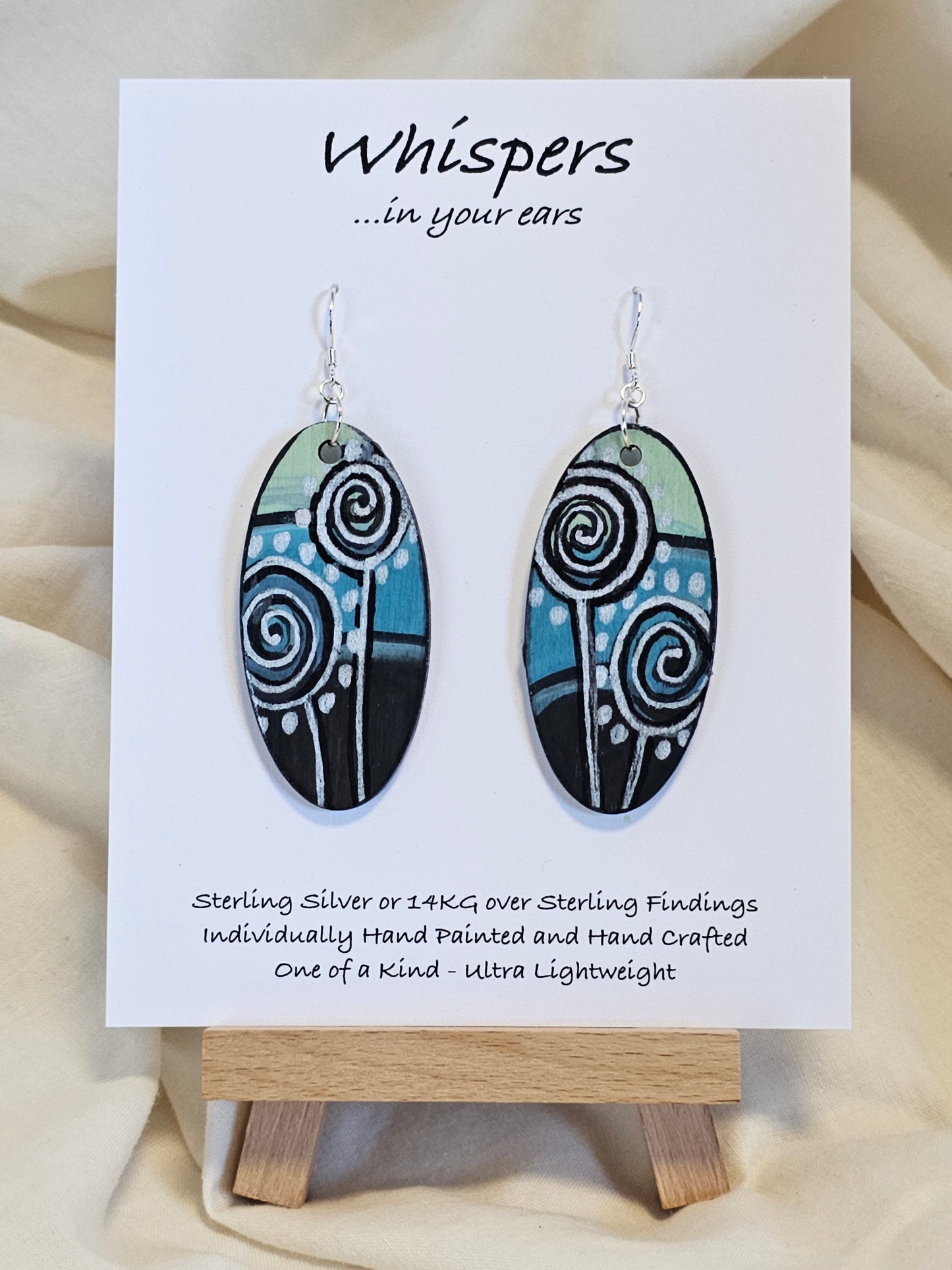 Silver Dandelion Puffball Hand Painted Wood Earrings. Geometric background in soft green, aqua blue and black. Back painted in similar design. Resin coated for durability. 2" Elongated oval wood. Sterling silver findings and hangs 2 1/4"