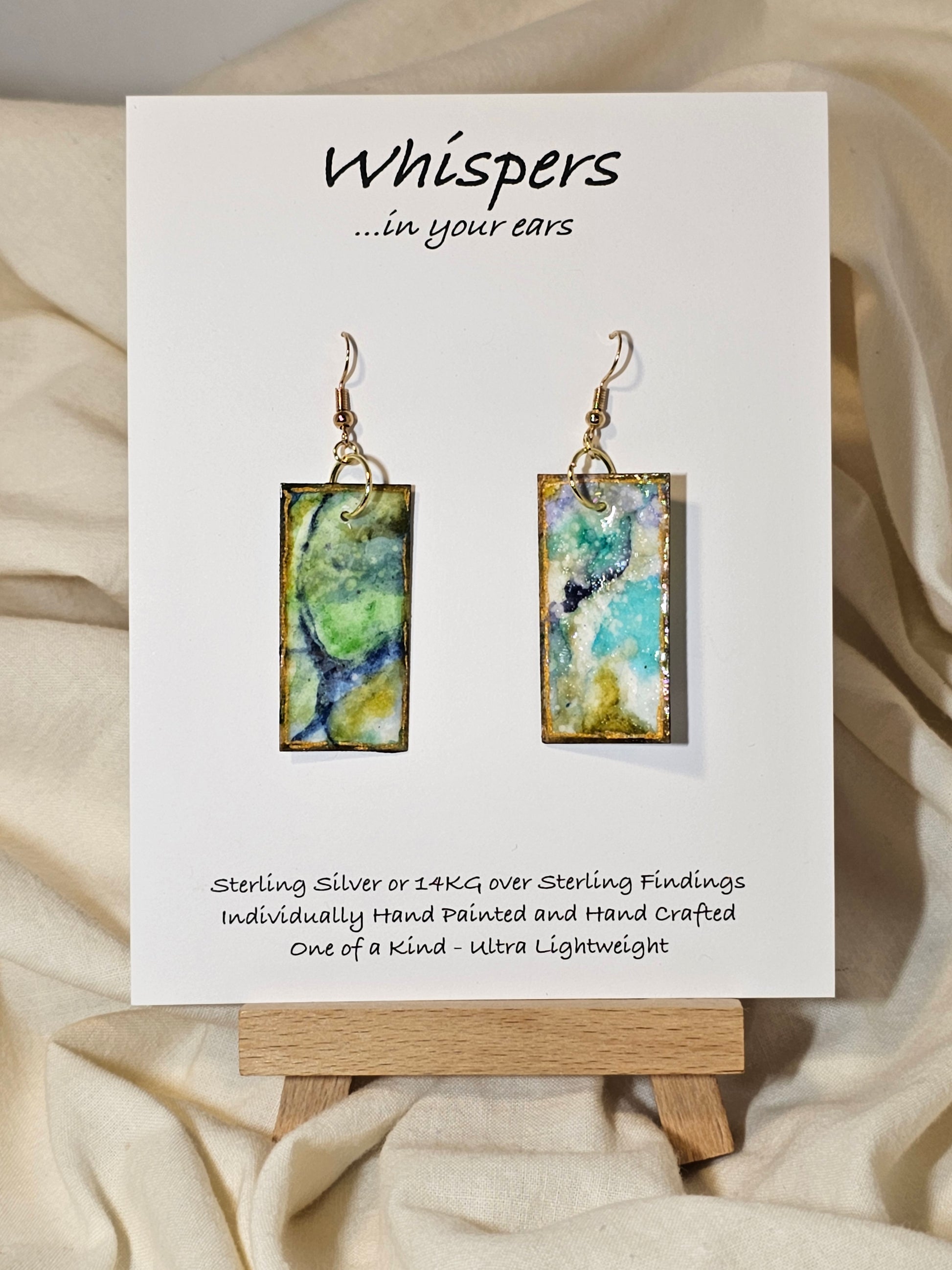 Land and Sea Abstract Hand Painted Paper Earrings. 3/4" x 1 1/2" Rectangle painted in watercolor on paper. Resin coated for durability. Mossy green, light green and blues. Edged in gold. Back is painted in similar design. 14kg over sterling silver ear wires and findings. Hangs 1 3/4"