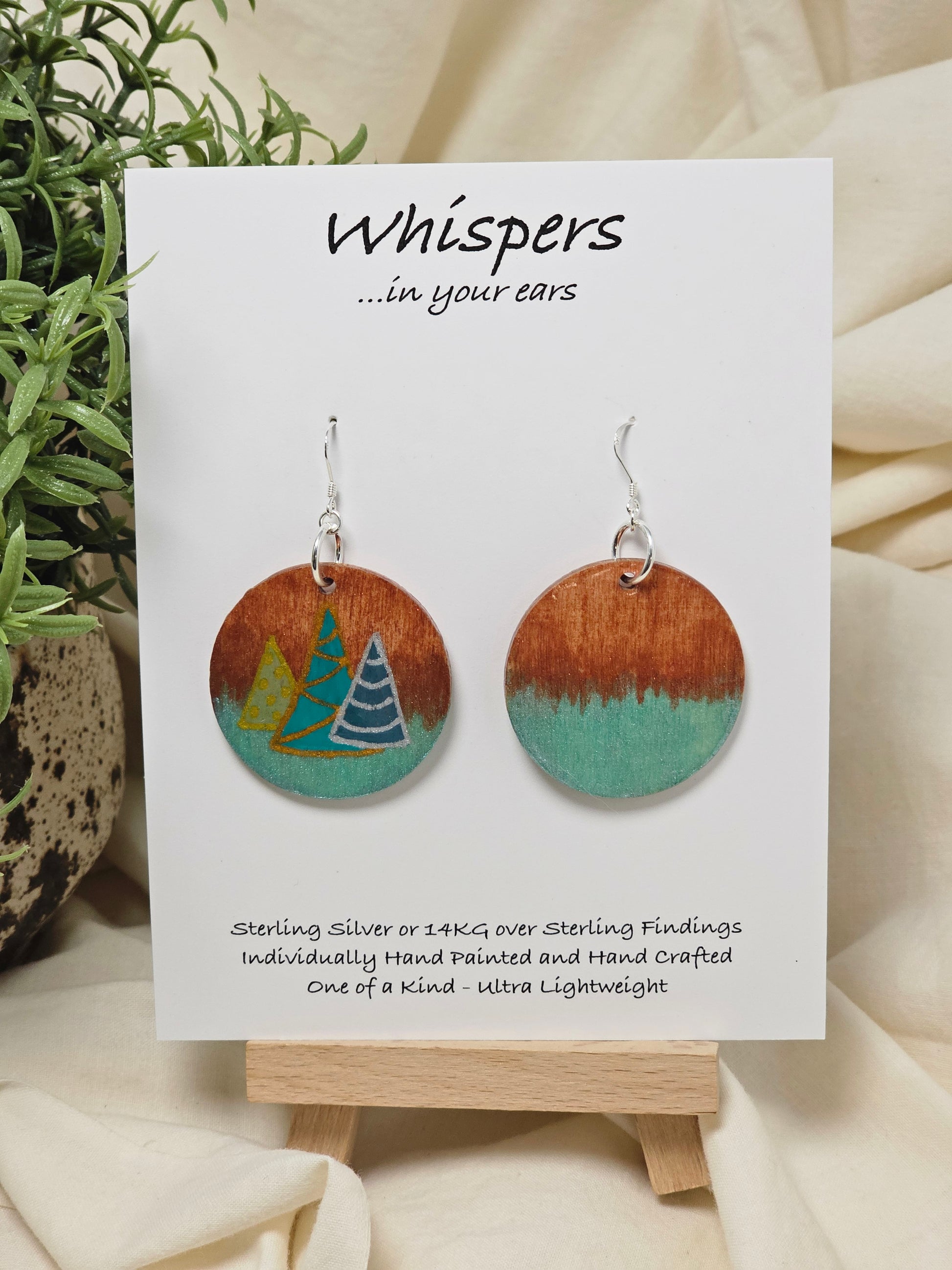 Three Modern Trees Hand Painted Wood Earrings. 1 1/2" wood round, two toned 3 Holiday trees painted with metallic colors .Back of earring is painted with copper and light iridescent green. Resin coated for durability. Sterling Silver findings. Hangs 1 3/4"