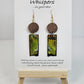Copper, Green and Black Abstract Motif Hand Painted Paper and Wood Earrings. 1/2" x 1 5/8" Paper Rectangle hand painted brightly colored background with silver and copper accents. Edged in black. Hanging from embellished wooden disc dark brown. Back is painted to match. Resin coating for durability. Sterling Silver findings. Hangs 2 1/2" in length