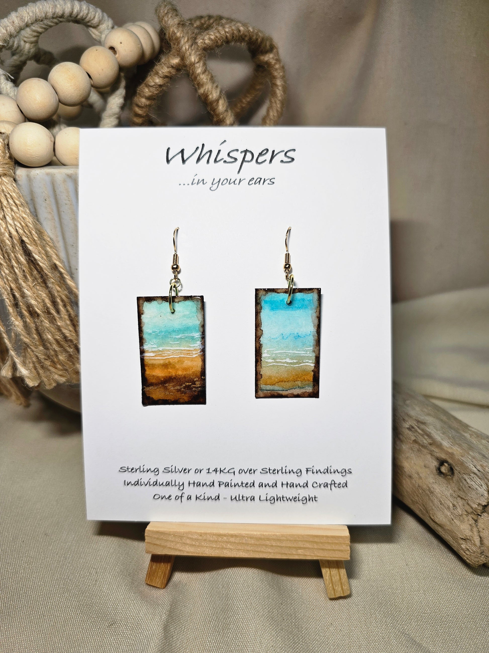 Metallic Beach Hand Painted Paper Earrings. Ultra lightweight 3/4" x 1 1/2" rectangle painted with watercolor. Depicts impressionistic beachscape. Metallic accents in sand. Edges painted in dark brown to frame the scene. Back is painted with the same design. Resin coating for durability. 14kg over sterling silver ear wires. Mixed metals. Hangs 1 3/4" in length