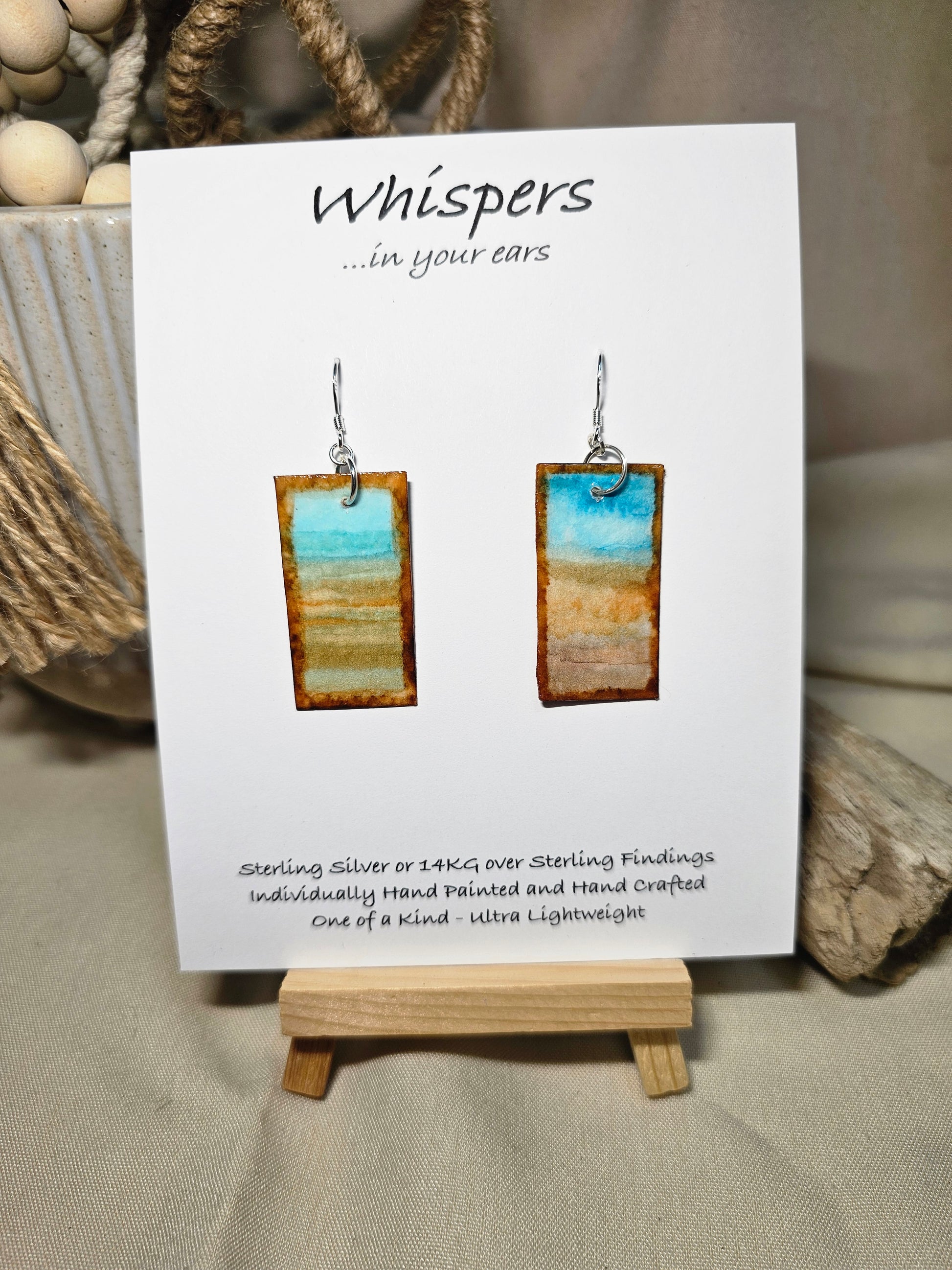 Beach Impressions Hand Painted Paper Earrings. Ultra lightweight 3/4" x 1 1/2" rectangle painted with watercolor. Depicts impressionistic beachscape. Subtle ocean color accents. Edges painted in brown to frame the scene. Back is painted with the same design. Resin coating for durability. Sterling silver ear wires. Hangs 1 3/4" in length