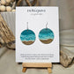 Shore Break Hand Painted Wood Earrings. 1 1/2" wooden round, Beach shoreline landscape painted with acrylics in aqua blues, teal and white. Ultra light weight. Back of earring is painted with similar design. Enameled for durability. Sterling silver ear wires and findings. Hangs 1 3/4"