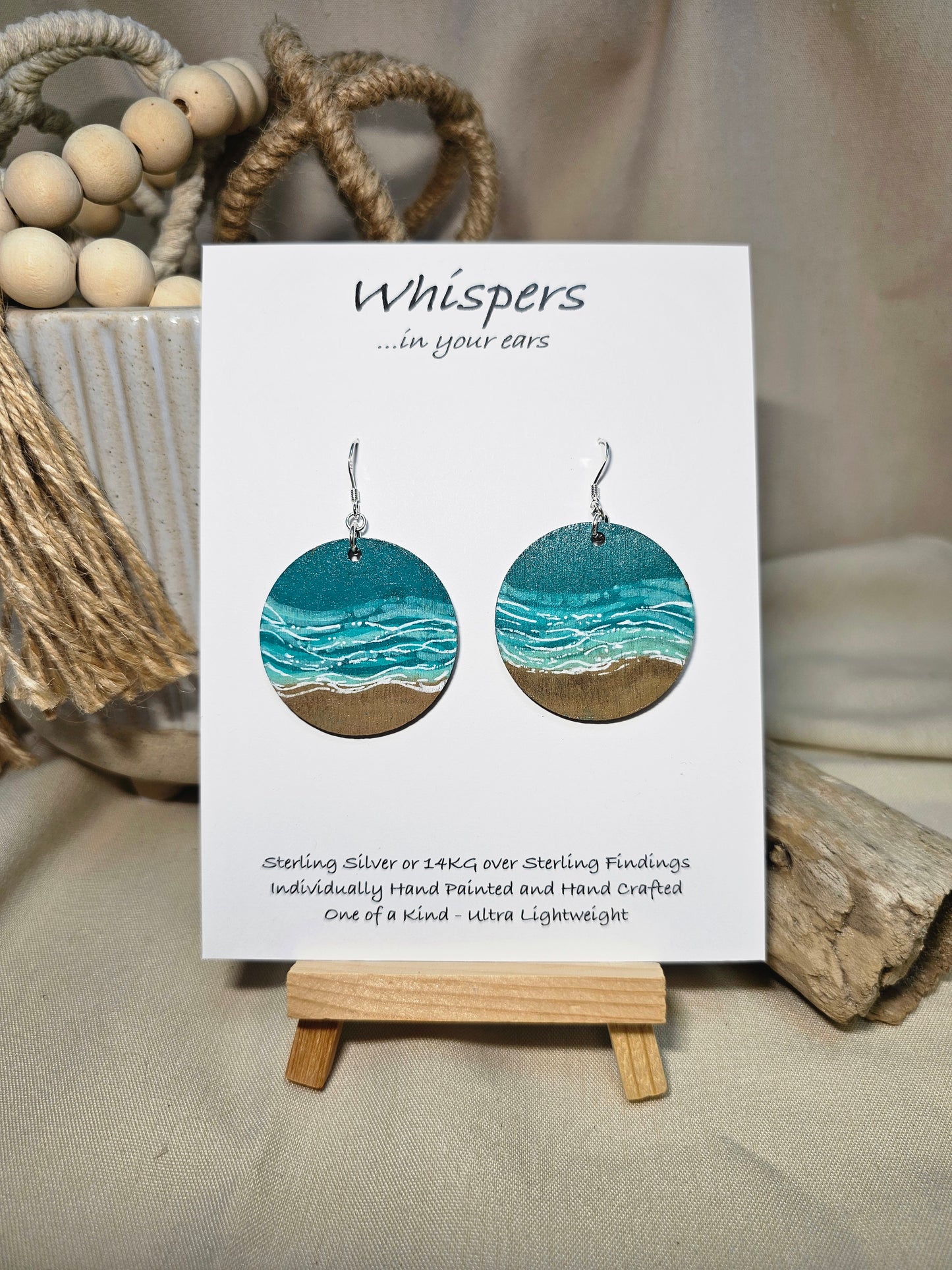 Shore Break Hand Painted Wood Earrings. 1 1/2" wooden round, Beach shoreline landscape painted with acrylics in aqua blues, teal and white. Ultra light weight. Back of earring is painted with similar design. Enameled for durability. Sterling silver ear wires and findings. Hangs 1 3/4"