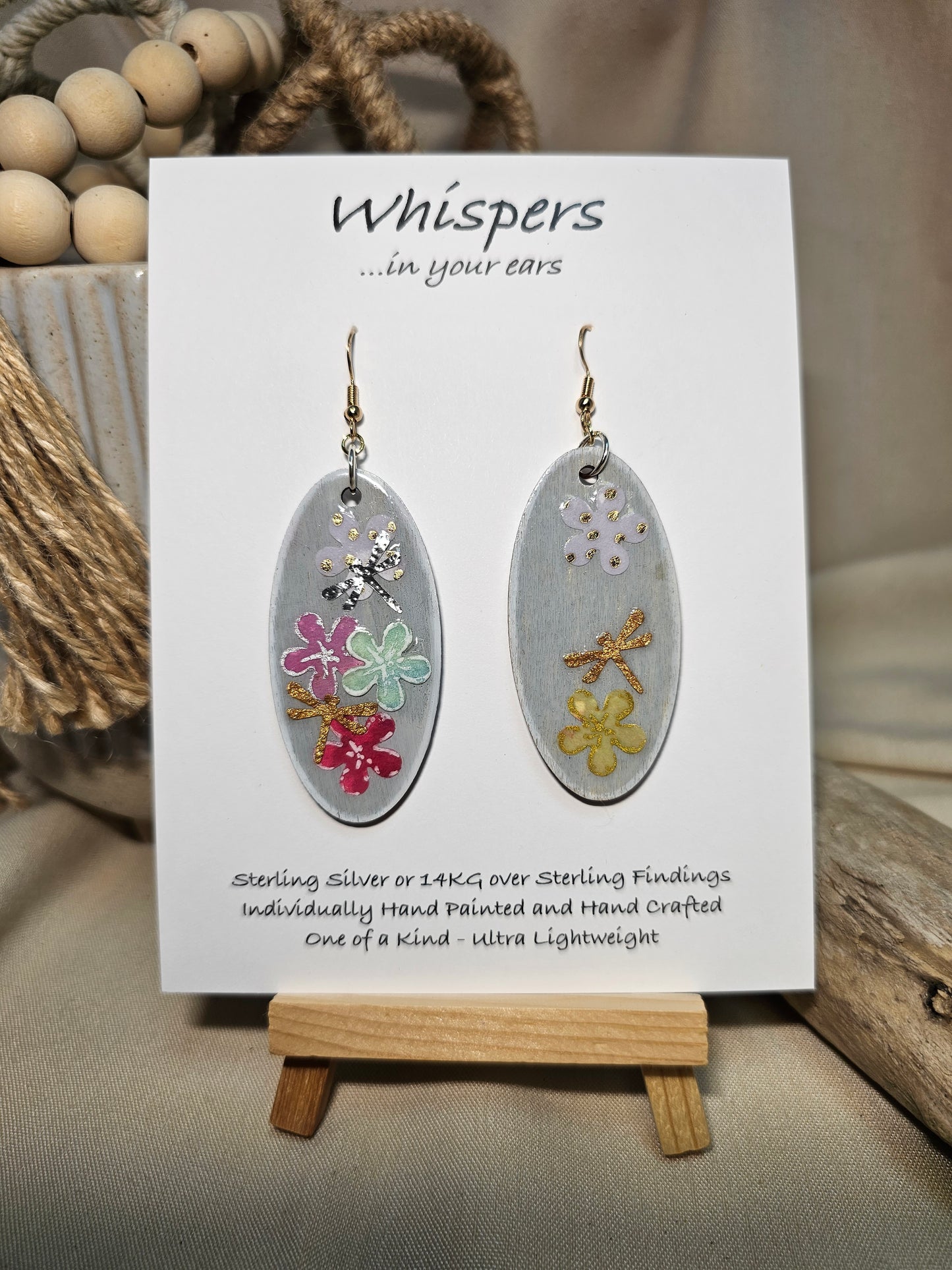 Vertical Floral Collage Bouquet, Hand Painted Wood Earrings. 3D painted flowers and a hand textured aluminum dragonfly. Front and back is painted light grey background. Enameled for durability. 2" Elongated wood oval. 14kg over sterling silver mixed metals with sterling silver findings and hangs 2 1/4" in length