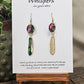 Jungle Pattern Feather Hand Painted Paper Earrings. 5/8" circular hand painted paper earring. Below hangs a gorgeous light weight metal enameled feather charm pendant. Back is gold in color. Pink, purple, gold, green, black and white, metallic accents edged in gold. Back of paper is painted in similar design and colors. Resin coated for durability. 14kg over sterling silver ear wires and findings. Hangs 2 1/2" in length