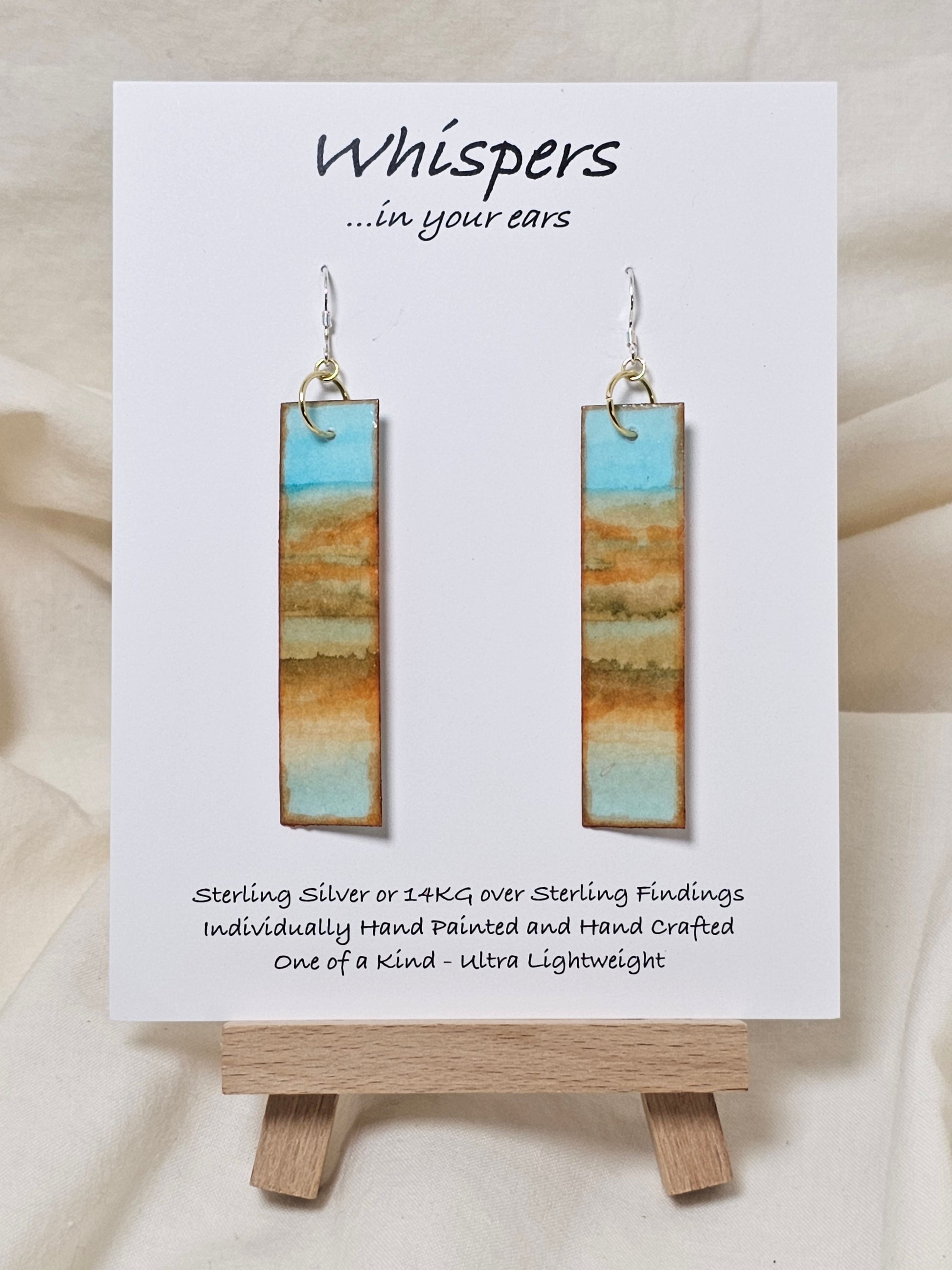Beachscape Reflection Statement Hand Painted Paper Earrings. Abstract beachscape painted in and on heavy watercolor paper. 1/2" x 2 1/2" elongated rectangle. In muted blues and beiges and corals. Reflection of landscape. Resin coating for durability. Sterling silver ear wires and findings. Ultra lightweight. Hangs 2 3/4"