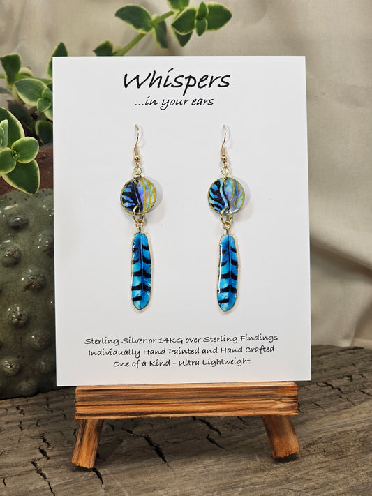 Black Feathers Hand Painted Paper Earrings. 5/8" circular hand painted paper earring. Below hangs a gorgeous light weight metal enameled feather charm pendant. Back is gold in color. Aqua blue, royal blue, black and white, metallic accents edged in gold. Back of paper is painted in similar design and colors. Resin coated for durability. 14kg over sterling silver ear wires and findings. Hangs 2 1/2" in length