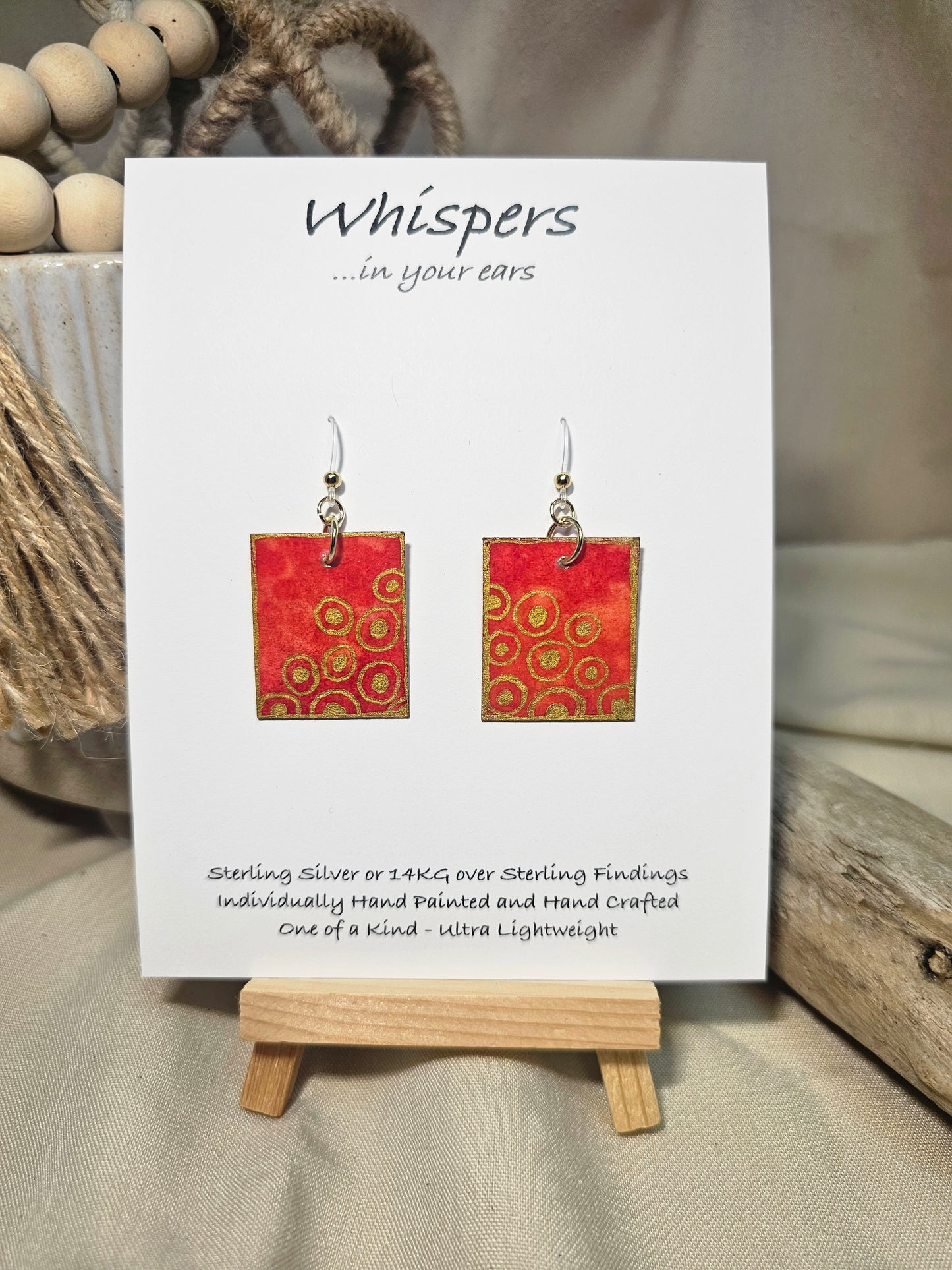 Concentric Gold Hand Painted Paper Earrings. Ultra lightweight 1" x 1 1/4" rectangle painted with Red and orange watercolor . Metallic gold circle design. Back is painted with the same design. Resin coating for durability. Acrylic ear wires. Hangs 1 1/2" in length