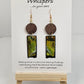 Copper, Green and Black Abstract Motif Hand Painted Paper and Wood Earrings. 1/2" x 1 5/8" Paper Rectangle hand painted brightly colored background with silver and copper accents. Edged in black. Hanging from embellished wooden disc dark brown. Back is painted to match. Resin coating for durability. Sterling Silver findings. Hangs 2 1/2" in length
