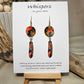 Gold Dot Feathers Hand Painted Paper Earrings. 3/4" circular hand painted paper earring. Below hangs a gorgeous light weight metal enameled feather charm pendant. Back is gold in color. Reds, blues, metallic accents edged in gold. Back of paper is painted in similar design and colors. Resin coated for durability. 14kg over sterling silver ear wires and findings. Hangs 2 1/2" in length