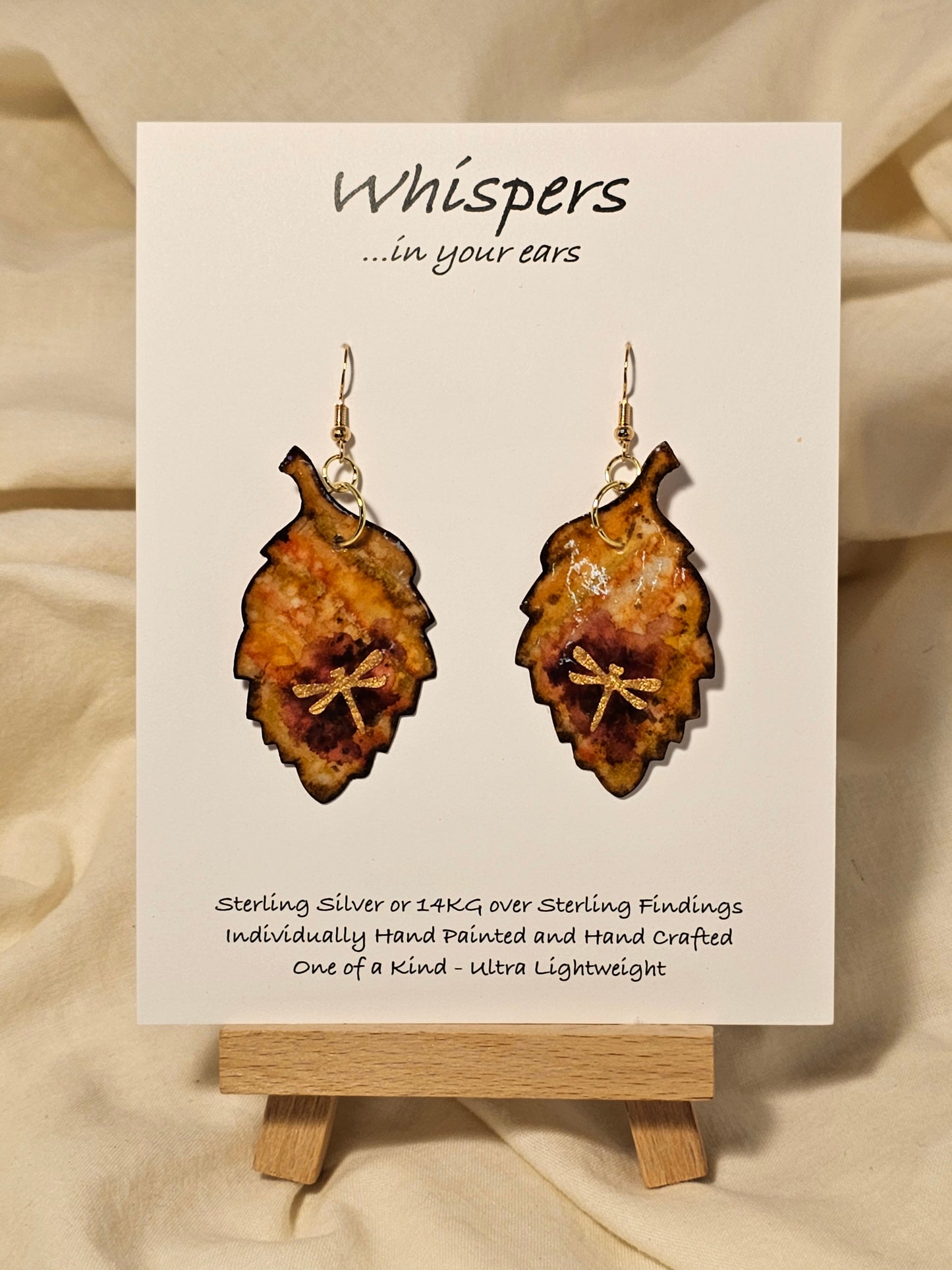Golden Dragonfly Leaf Hand Painted Paper Earrings. Ultra light weight. 2" Leaf shape. Painted in rust and muted red tones with Golden paper dragonfly atop. Outlined in Dark brown. Back is painted in similar design. 14kg over Sterling Silver ear wires and findings. Resin coating for durability. Hangs 2"