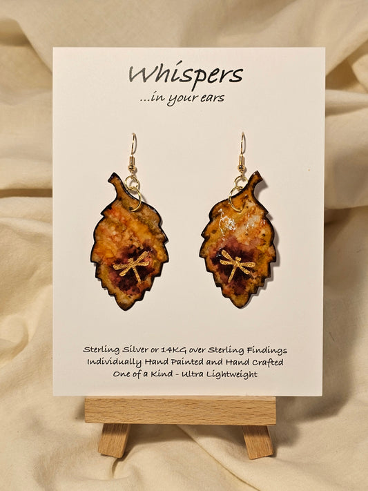Golden Dragonfly Leaf Hand Painted Paper Earrings. Ultra light weight. 2" Leaf shape. Painted in rust and muted red tones with Golden paper dragonfly atop. Outlined in Dark brown. Back is painted in similar design. 14kg over Sterling Silver ear wires and findings. Resin coating for durability. Hangs 2"