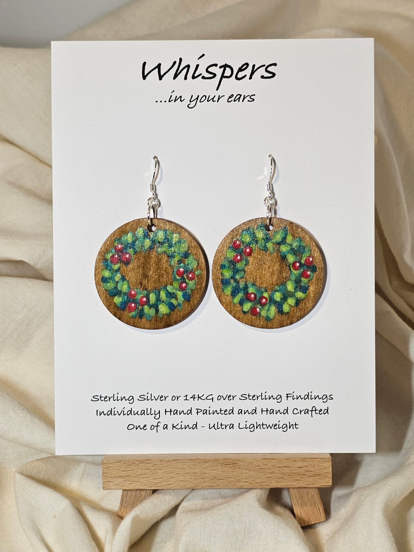 Holly Wreath Hand Painted Wood Earrings. 1 1/2" Stained wood round, two toned Holiday wreath painted with red berries. Back of earring is stained. Enameled for durability. Sterling Silver findings. Hangs 1 3/4"