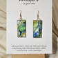 Land and Sea Abstract Hand Painted Paper Earrings. 3/4" x 1 1/2" Rectangle painted in watercolor on paper. Resin coated for durability. Mossy green, light green and blues. Edged in gold. Back is painted in similar design. 14kg over sterling silver ear wires and findings. Hangs 1 3/4"