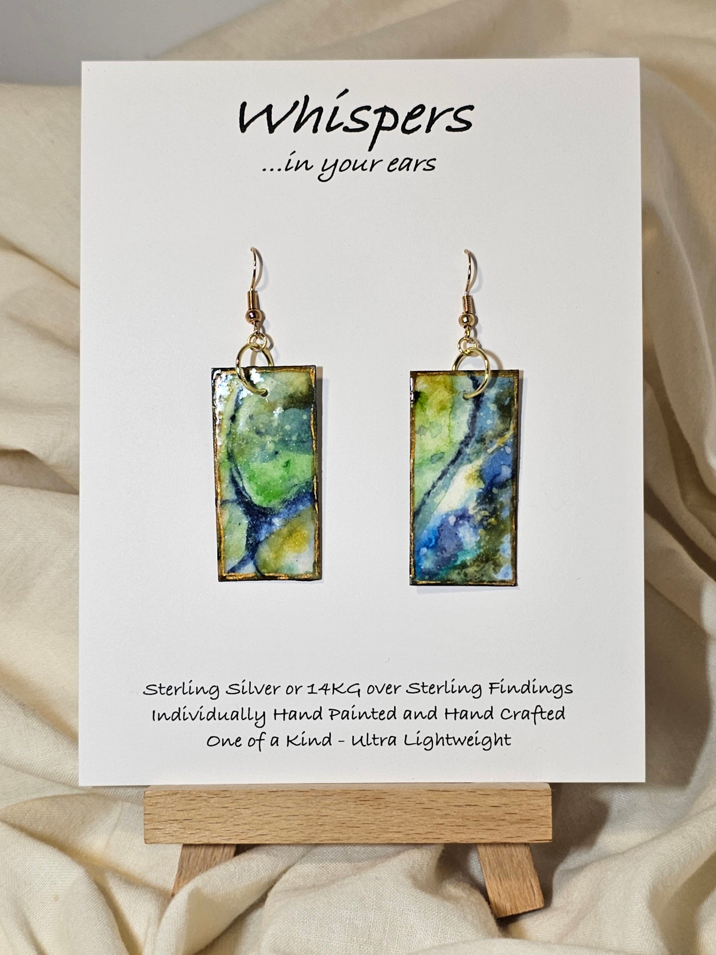 Land and Sea Abstract Hand Painted Paper Earrings. 3/4" x 1 1/2" Rectangle painted in watercolor on paper. Resin coated for durability. Mossy green, light green and blues. Edged in gold. Back is painted in similar design. 14kg over sterling silver ear wires and findings. Hangs 1 3/4"