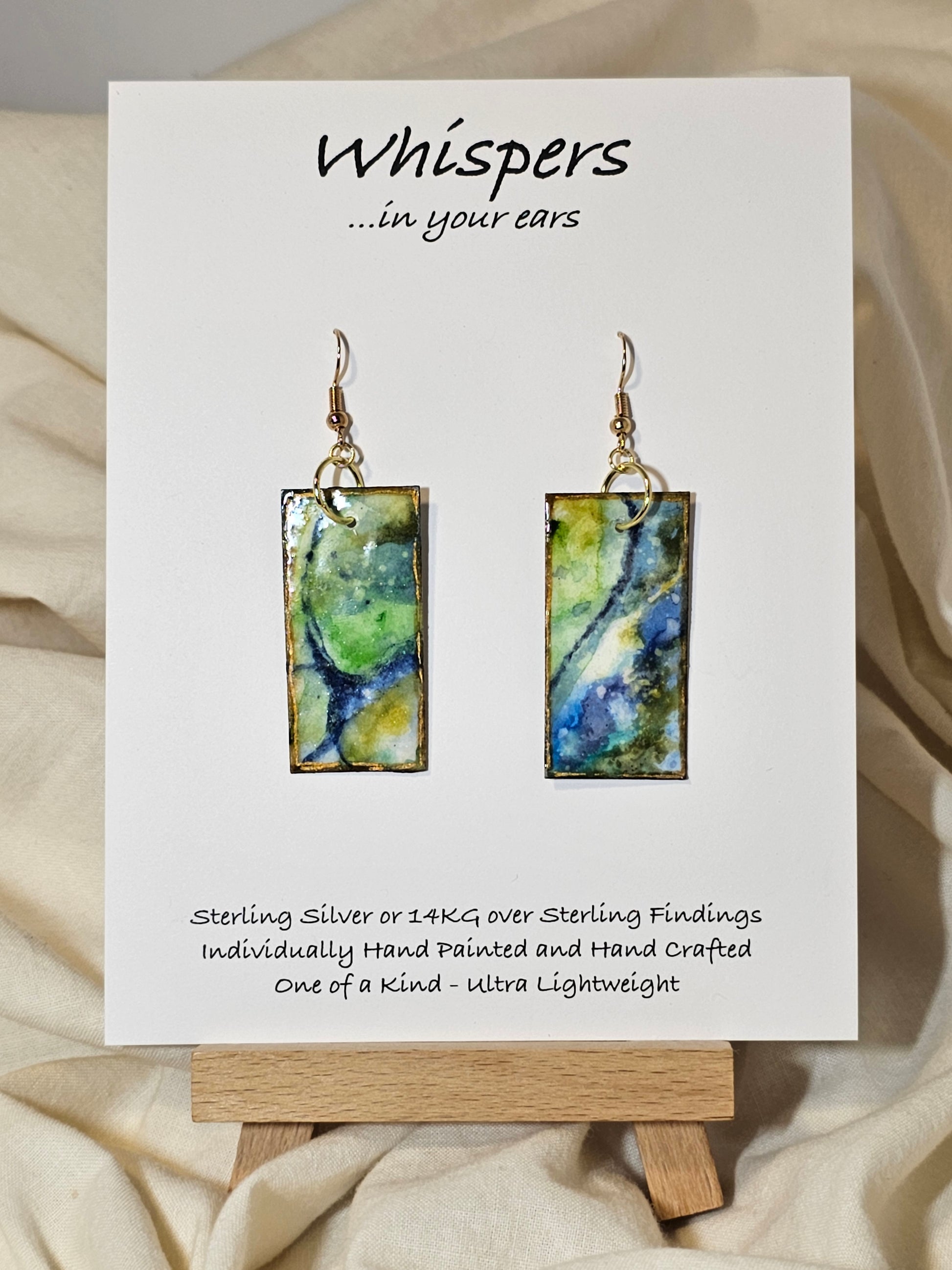 Land and Sea Abstract Hand Painted Paper Earrings. 3/4" x 1 1/2" Rectangle painted in watercolor on paper. Resin coated for durability. Mossy green, light green and blues. Edged in gold. Back is painted in similar design. 14kg over sterling silver ear wires and findings. Hangs 1 3/4"
