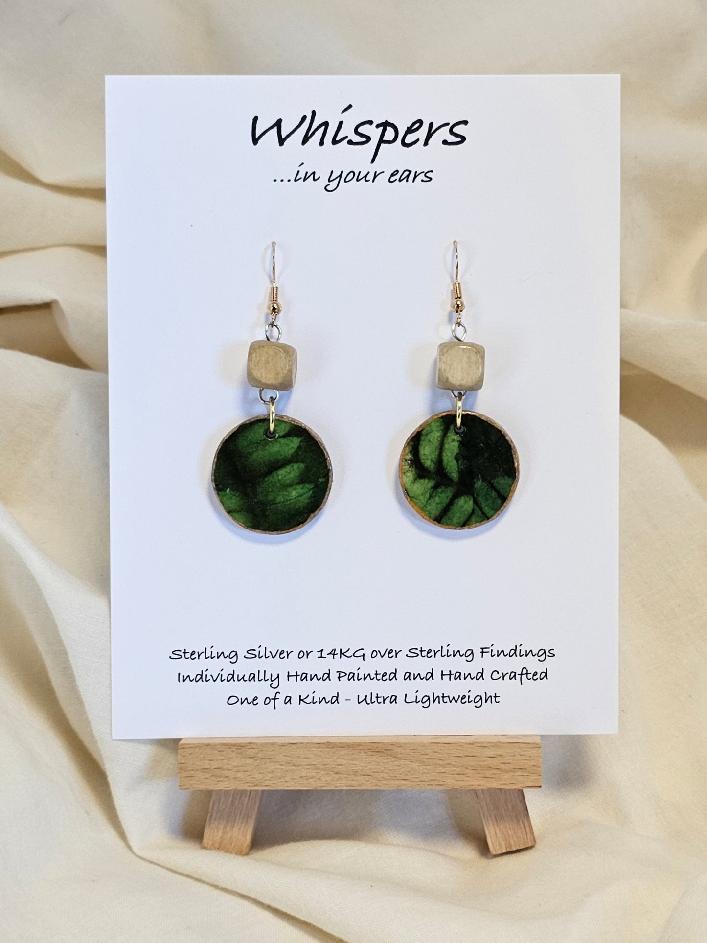 Leaf Relief Hand Crafted Wood Earrings. 1" Wood Disc with two tone green handmade paper painted gold edges and hanging from cream colored square wooden bead. Resin Coating for durability. Back is done to compliment. 14kg over sterling ear wire sterling silver findings. Hangs 1 3/4"