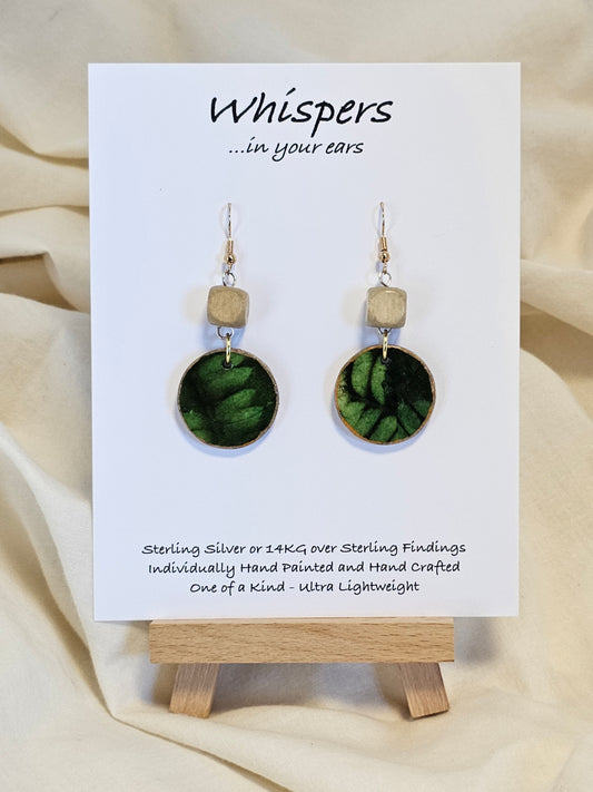 Leaf Relief Hand Crafted Wood Earrings. 1" Wood Disc with two tone green handmade paper painted gold edges and hanging from cream colored square wooden bead. Resin Coating for durability. Back is done to compliment. 14kg over sterling ear wire sterling silver findings. Hangs 1 3/4"