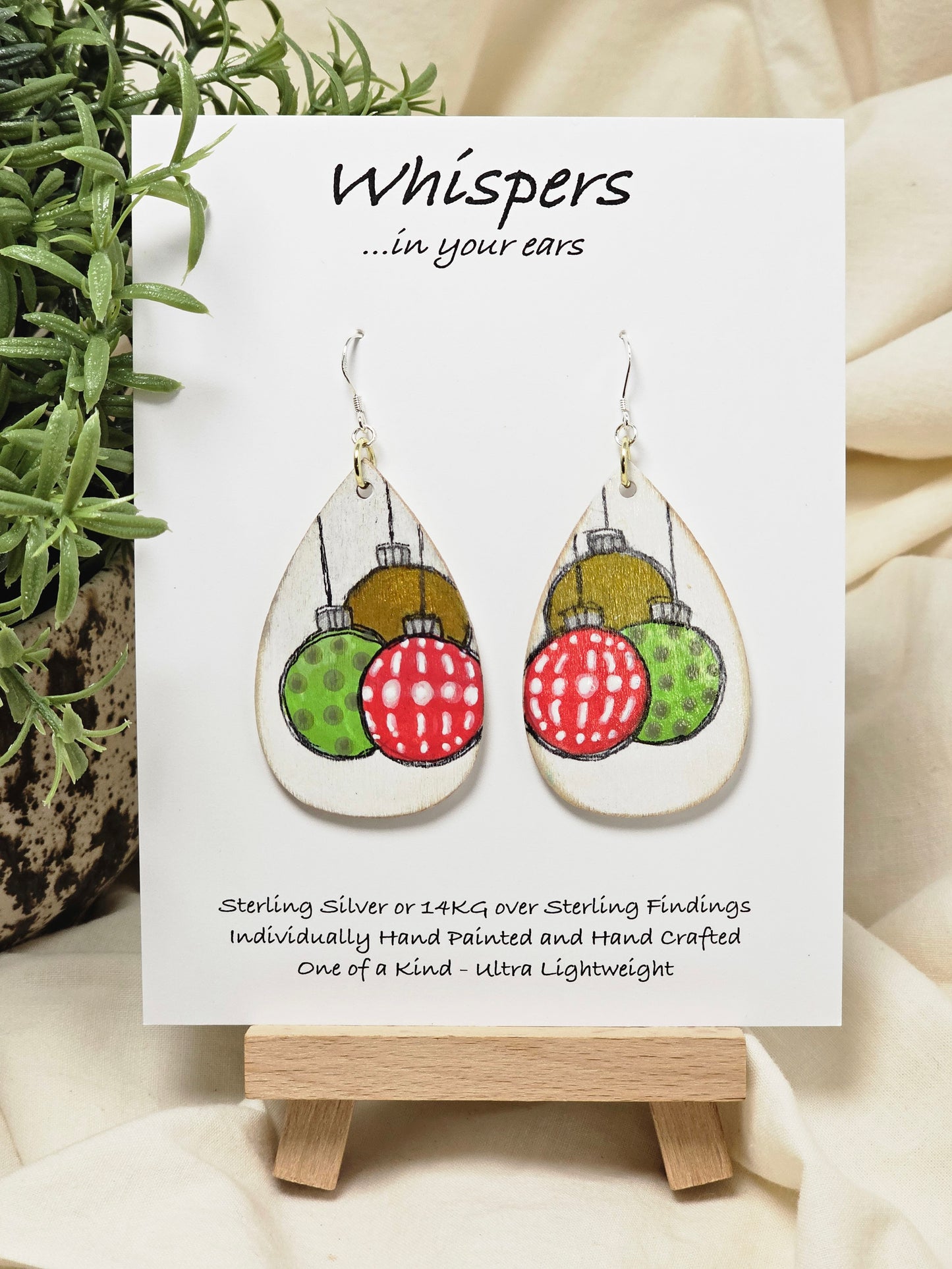 Ornament Trio Hand Painted Wood Earrings. 2" Wood Tear Drop painted white background. Three hand painted. Pattern Ornaments painted red, green and copper, outlined in black. Back is painted white. Distressed edge. Enameled for durability. Sterling Silver ear wires and findings. Ultra light weight. Hangs 2 1/2"