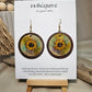 Sunflower Wash Hand Painted Wood Earrings. 1 1/2" wooden round. Hangs inside larger dark stained wood circle pendant. Sunflower painted in watercolor. Yellow, aqua blues, green and brown. Ultra light weight. Back of earring is painted with similar design. Enameled for durability. 14kg over Sterling silver ear wires and findings. Hangs 2"
