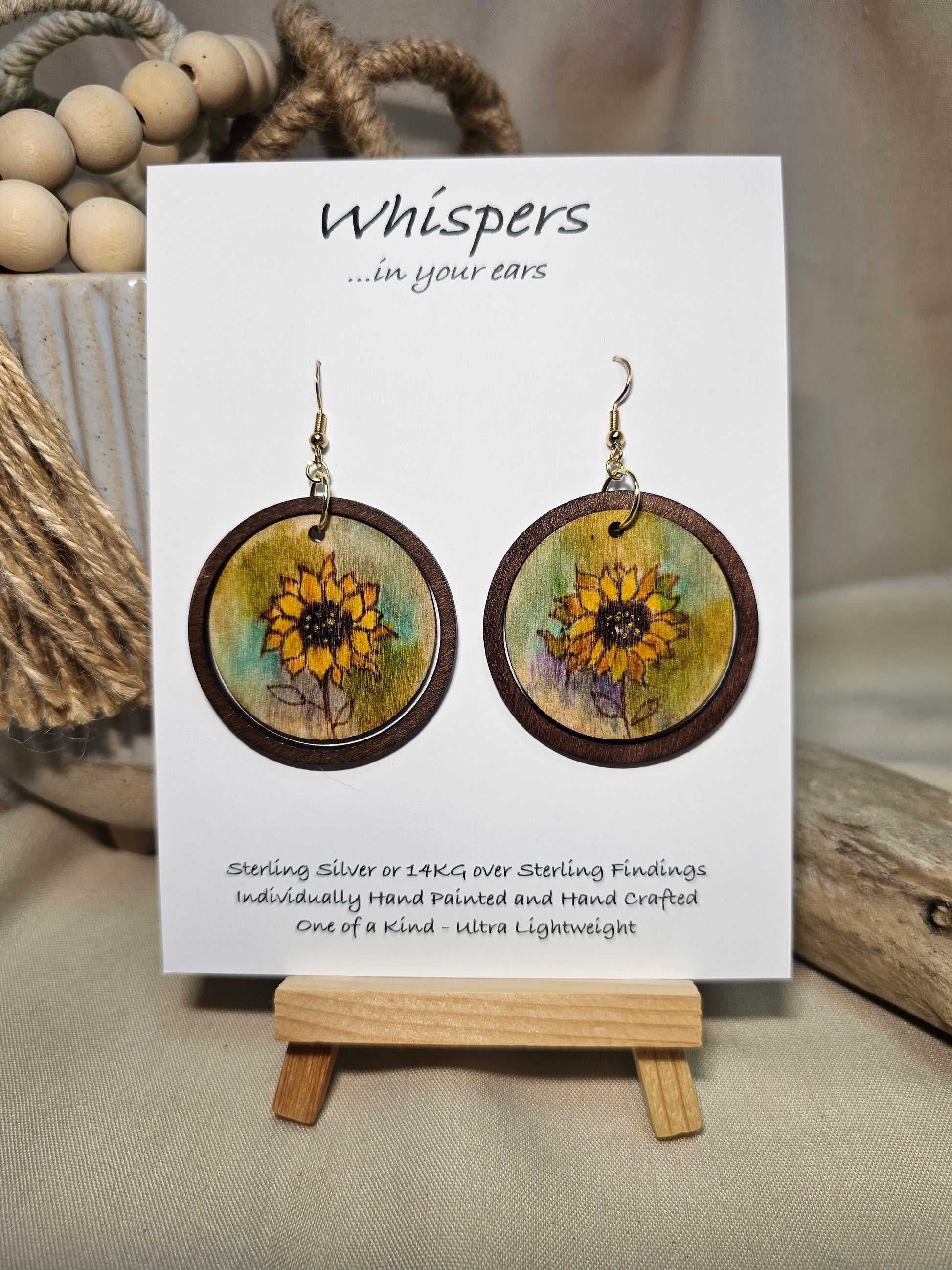 Sunflower Wash Hand Painted Wood Earrings. 1 1/2" wooden round. Hangs inside larger dark stained wood circle pendant. Sunflower painted in watercolor. Yellow, aqua blues, green and brown. Ultra light weight. Back of earring is painted with similar design. Enameled for durability. 14kg over Sterling silver ear wires and findings. Hangs 2"