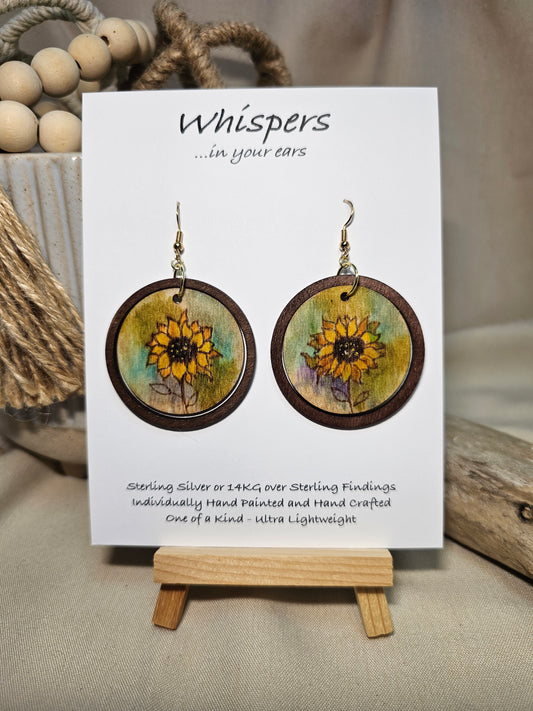 Sunflower Wash Hand Painted Wood Earrings. 1 1/2" wooden round. Hangs inside larger dark stained wood circle pendant. Sunflower painted in watercolor. Yellow, aqua blues, green and brown. Ultra light weight. Back of earring is painted with similar design. Enameled for durability. 14kg over Sterling silver ear wires and findings. Hangs 2"