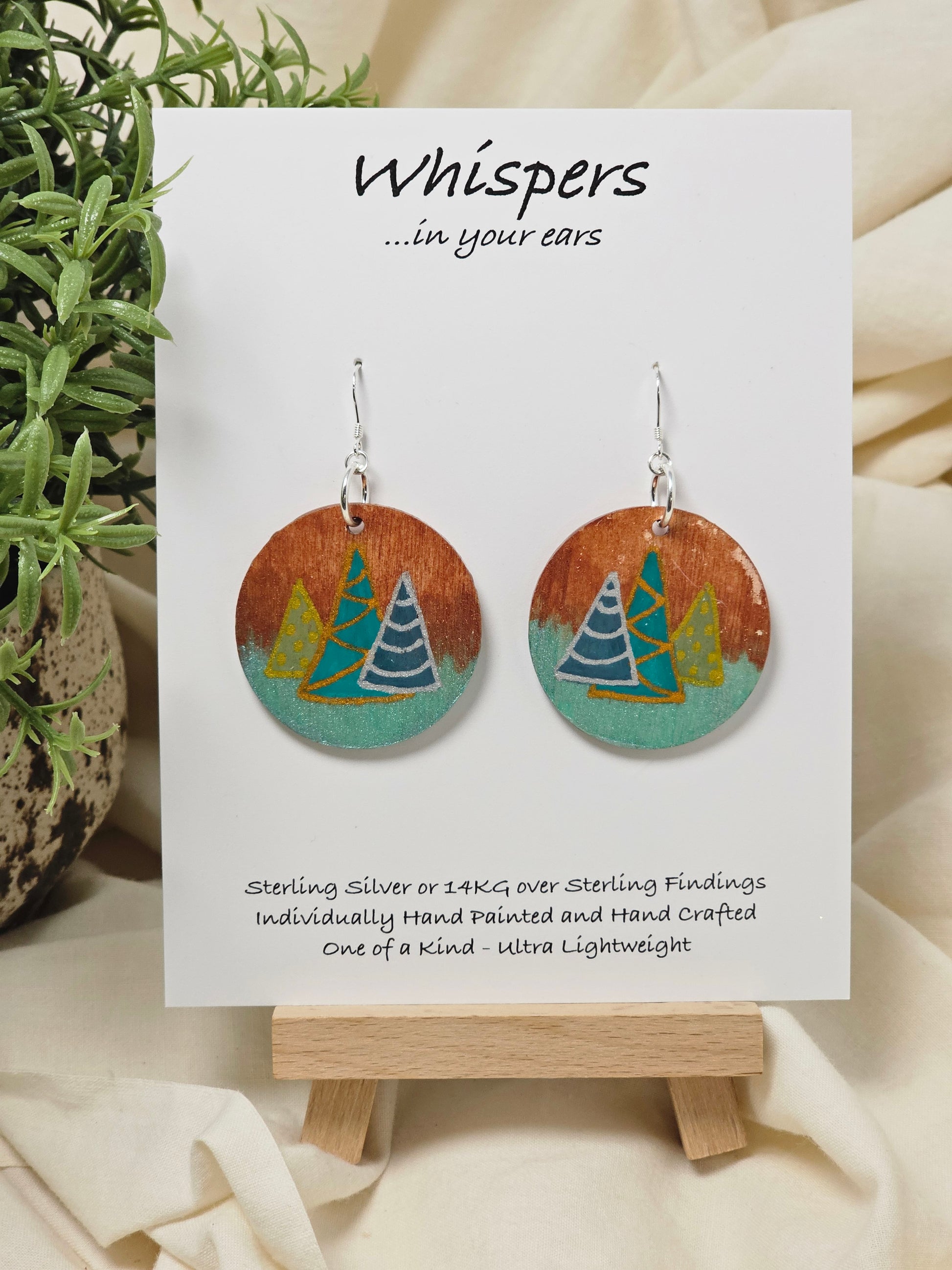 Three Modern Trees Hand Painted Wood Earrings. 1 1/2" wood round, two toned 3 Holiday trees painted with metallic colors .Back of earring is painted with copper and light iridescent green. Resin coated for durability. Sterling Silver findings. Hangs 1 3/4"