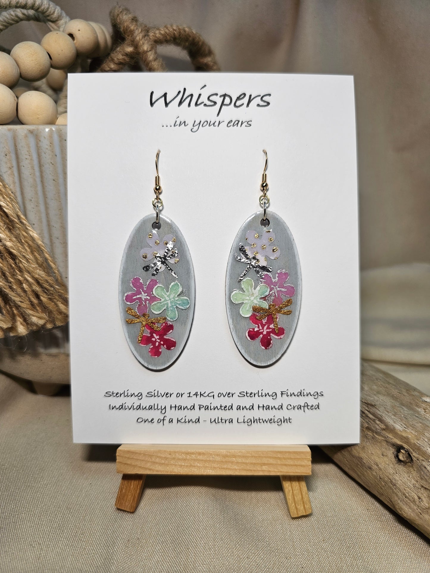 Vertical Floral Collage Bouquet, Hand Painted Wood Earrings. 3D painted flowers and a hand textured aluminum dragonfly. Front and back is painted light grey background. Enameled for durability. 2" Elongated wood oval. 14kg over sterling silver mixed metals with sterling silver findings and hangs 2 1/4" in length