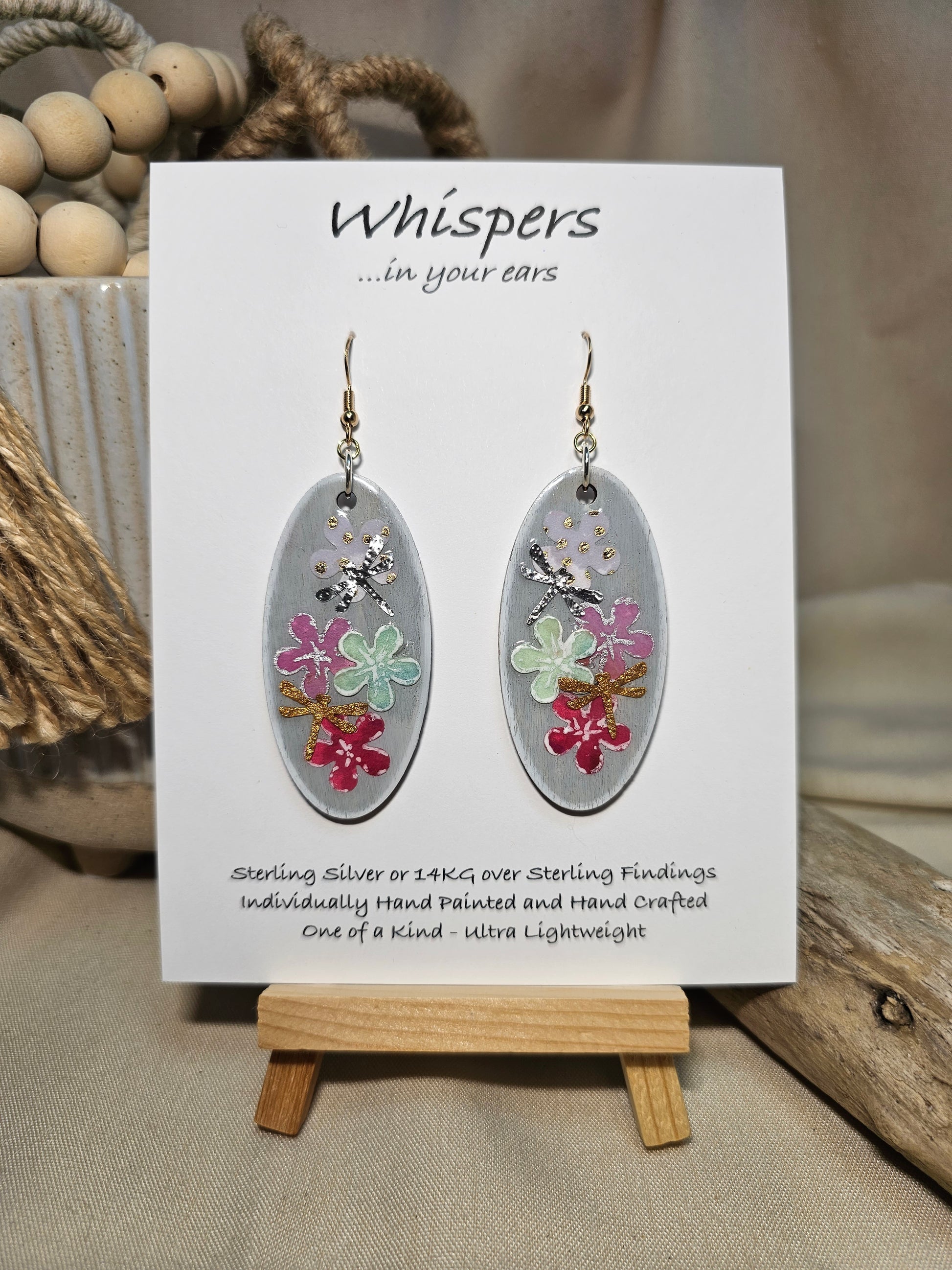 Vertical Floral Collage Bouquet, Hand Painted Wood Earrings. 3D painted flowers and a hand textured aluminum dragonfly. Front and back is painted light grey background. Enameled for durability. 2" Elongated wood oval. 14kg over sterling silver mixed metals with sterling silver findings and hangs 2 1/4" in length