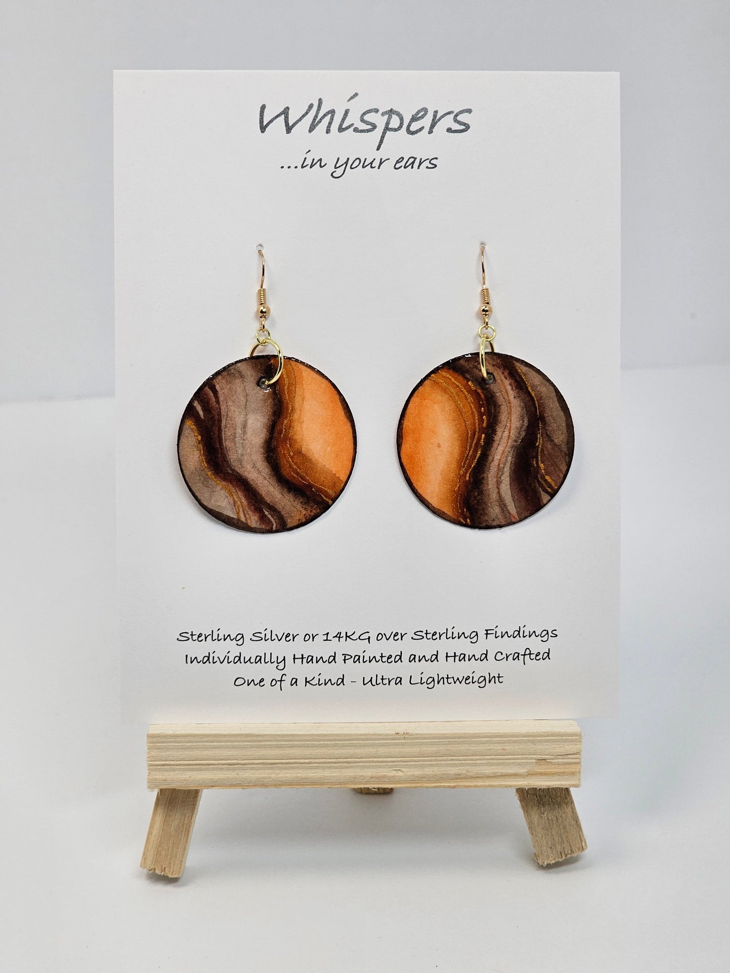 Wooden Glow Hand painted Paper earrings. Look of wood in bark pattern, orange glow and brown and dark brown lines. Gold metallic veining. Back of earring is painted to match. Ultra lightweight. Resin coated for durability. 1 1/2" diameter. 14KG over Sterling findings. Hangs 1 3/4" in length